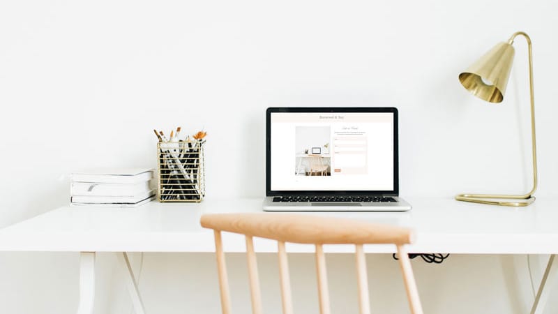 Image of a white desk on top of which is a lamp, a laptop and a container of pens. There is also a beechwood ladder back chair. Organically boost traffic.