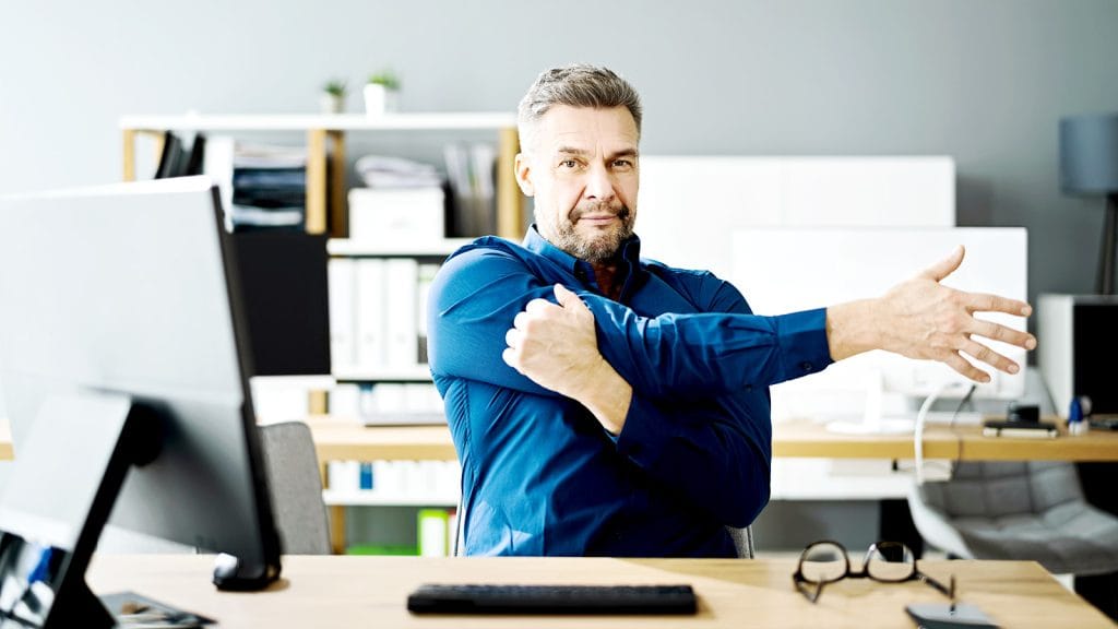 A desk worker stretching arms and shoulders at their desk.