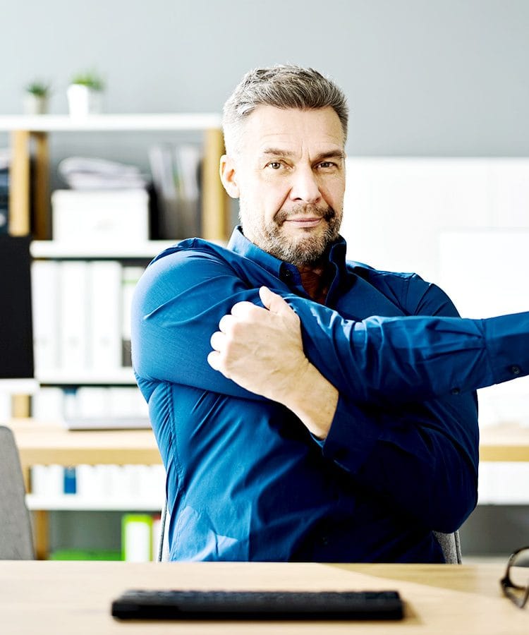A desk worker stretching arms and shoulders at their desk.