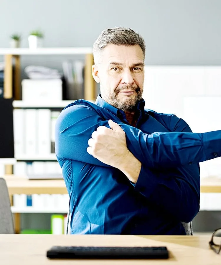 A desk worker stretching arms and shoulders at their desk.
