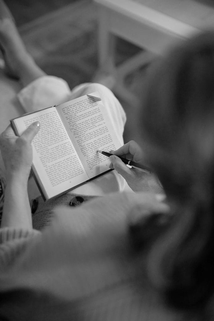 A black and white image of a woman reading and editing a small book.